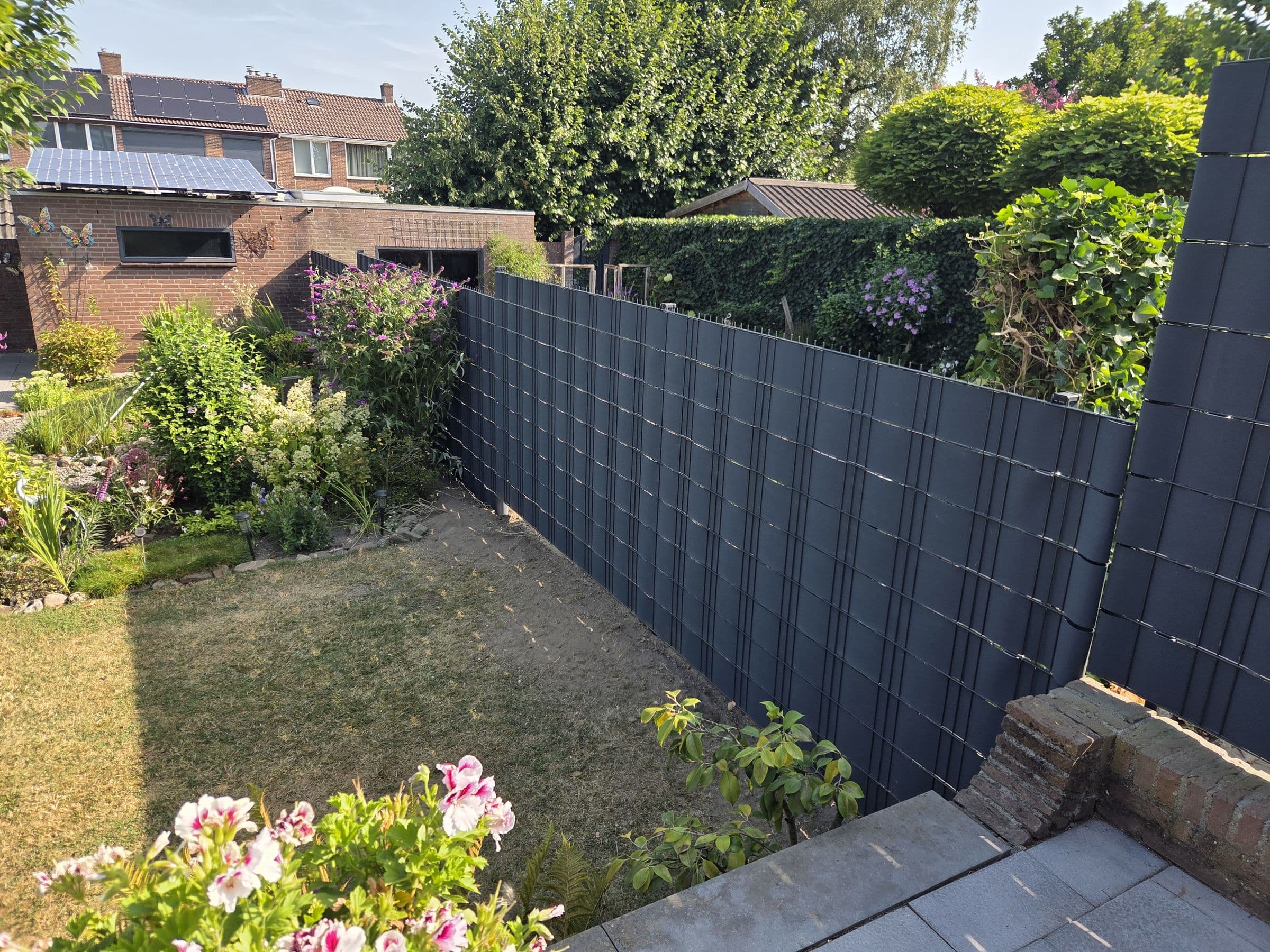Composiet antraciet: Antraciet schutting achter een bloementuin