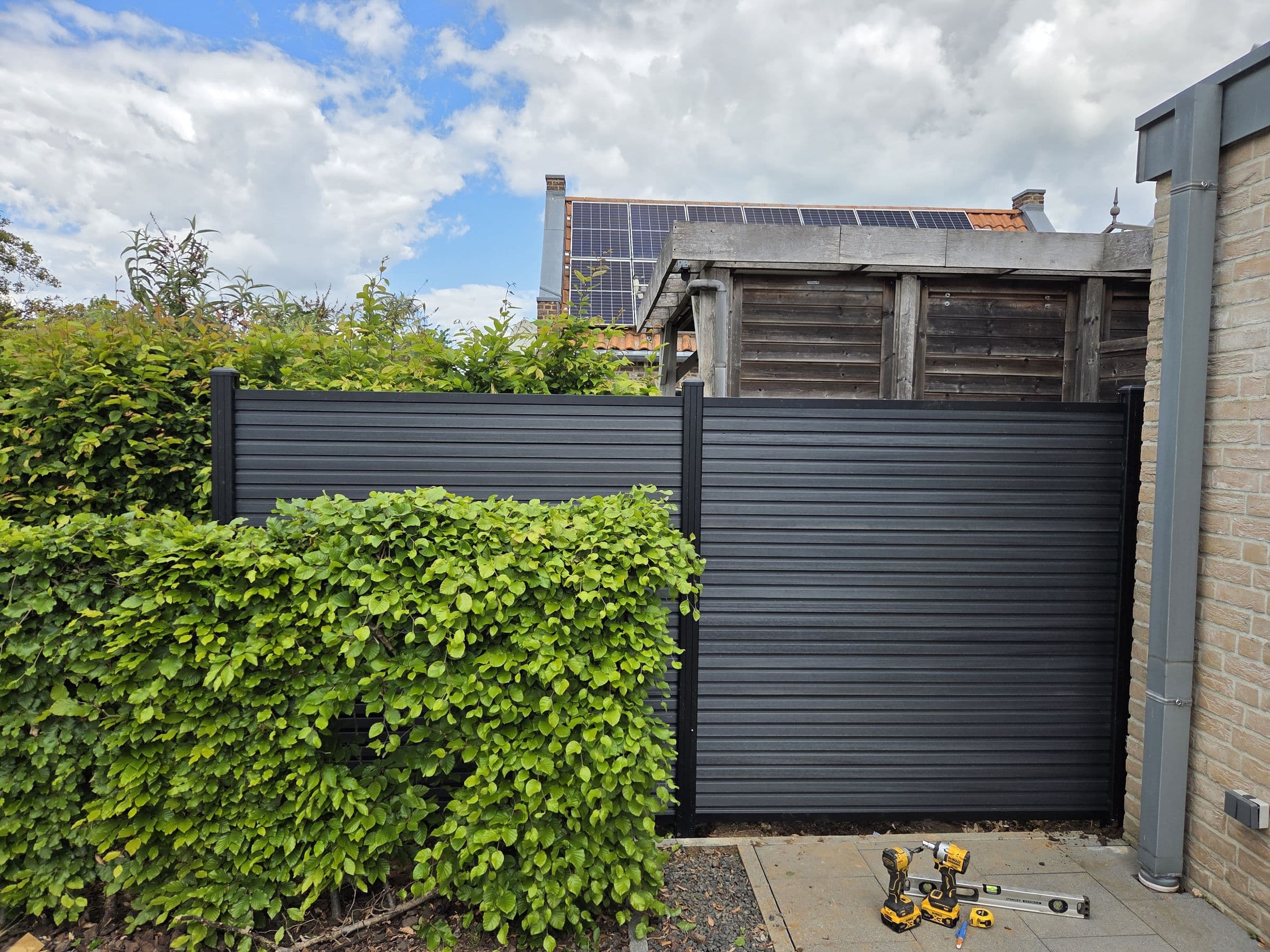 Composiet antraciet: Antraciet schutting met poort, achter een haag